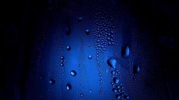 uma solta do água em uma vidro fechar-se macro com espumante bokeh em azul borrado fundo. abstrato solta água. gota de chuva deslizar baixa a janela vidro, formando abstrato figura video