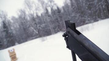 en man siktar en pellets pistol mot en mål, praktiserande hans syfte i de vinter. klämma. de skytten i kamouflage mål en mål med en gevär med ett optisk syn, fokus på vapen. video