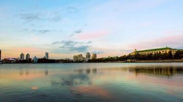 cênico panorama paisagem urbana, cidade refletido em lago às pôr do sol. vídeo. urbano noite cena. panorama do cidade costa do lago com edifícios fundo e pôr do sol video