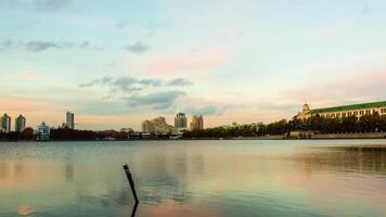 szenisch Panorama Stadtbild, Stadt reflektiert auf See beim Sonnenuntergang. Video. städtisch Nacht Szene. Panorama von Stadt Ufer von See mit Gebäude Hintergrund und Sonnenuntergang video