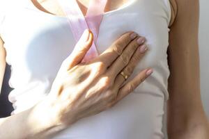 Disparo de el mujer en el blanco arriba, con rosado cinta en su cuello como un símbolo de pecho cáncer conciencia, ejecutando yo examen de el pechos, mirando para anormalidades. concepto foto