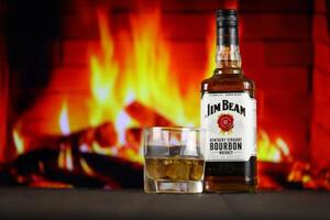 KYIV, UKRAINE - MAY 4, 2022 Jim Beam original alcohol bottle on wooden table with red fireplace photo