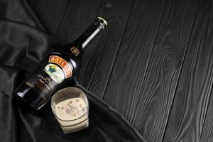 KYIV, UKRAINE - MAY 4, 2022 Baileys original alcohol bottle on wooden table with black fabric photo