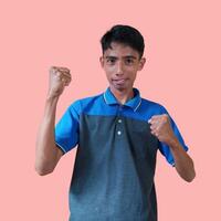 Excited Asian man wearing blue t-shirt pointing to top copy space, isolated pink background. photo