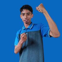 Excited Asian man wearing blue t-shirt pointing to top copy space, isolated blue background. photo