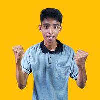 The enthusiastic face of the Asian youth clenched his fists. isolated on yellow background. photo