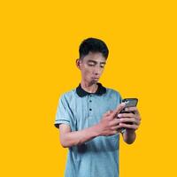emocionado asiático hombre participación inteligente teléfono vistiendo gris camiseta, amarillo antecedentes foto