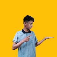Excited Asian man wearing gray t-shirt pointing at copy space on the side, isolated on yellow background. photo