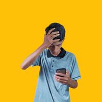 young asian man holding head and smart phone wearing gray t-shirt, yellow background. photo