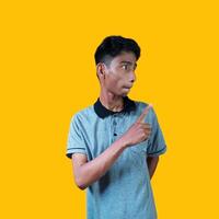 excited asian man wearing gray t-shirt pointing to the copy space on the side, isolated yellow background. photo