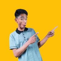 excited asian man wearing gray t-shirt pointing to the copy space on the side, isolated yellow background. photo