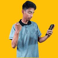 Excited Asian man wearing gray t-shirt pointing to copy space next to holding smart phone, isolated on yellow background. photo