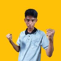 The enthusiastic face of the Asian youth clenched his fists. isolated on yellow background. photo