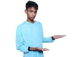 Excited Asian man wearing blue t-shirt pointing at copy space on the side, isolated on white background. photo