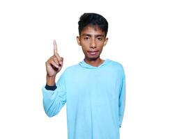 excited asian man wearing blue t-shirt pointing to the copy space on the side, isolated white background. photo