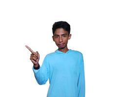 excited asian man wearing blue t-shirt pointing to the copy space on the side, isolated white background. photo