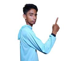 excited asian man wearing blue t-shirt pointing to the copy space on the side, isolated white background. photo