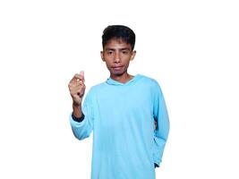 Young Asian man feeling happy and romantic forming heart gesture, wearing blue t-shirt on white background. photo