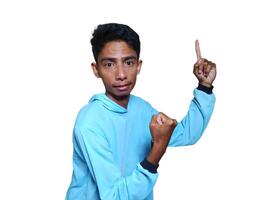 excited asian man wearing blue t-shirt pointing to the copy space on the side, isolated white background. photo