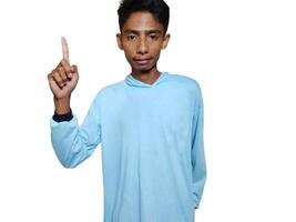 excited asian man wearing blue t-shirt pointing to the copy space on the side, isolated white background. photo