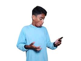 Young asian man surprised looking at mobile phone wearing blue t-shirt, white background photo