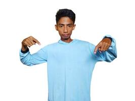 excited asian man wearing blue t-shirt pointing to the copy space on the side, isolated white background. photo