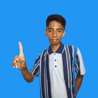 excited asian man wearing colorful t-shirt pointing to the copy space on the side, isolated blue background. photo