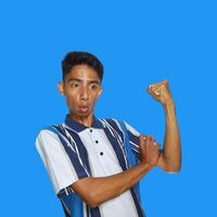 Excited Asian man wearing colorful t-shirt showing strong movement raising arms blue background. photo