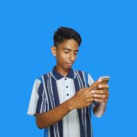 joven asiático hombre sorprendido mirando a inteligente teléfono en izquierda mano participación aislado azul antecedentes foto