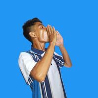 asian man shouting wearing colorful t-shirt, isolated blue background. photo