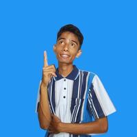 Outward looking young Asian man wearing colorful t-shirt, copy space index finger with new idea, isolated on blue background photo