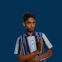 young asian man hands stop. with a serious face wearing a colorful t-shirt, isolated on a blue background photo