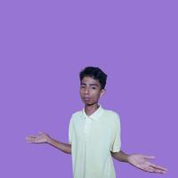 young asian man with a surprised face facing the camera, with both hands to the side, wearing a yellow blue t-shirt, isolated on a purple background photo