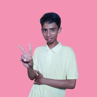 Young Asian man feeling happy and romantic forming heart gesture, wearing yellow t-shirt on pink background. photo