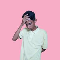 Dizzy face holding head of young Asian man in yellow shirt isolated on pink background photo