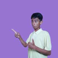 excited asian man wearing yellow t-shirt pointing to the copy space on the side, isolated purple background. photo