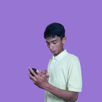 Young asian man surprised looking at smart phone, wearing yellow t-shirt, isolated purple background. photo