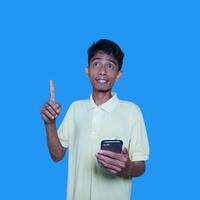 Young outward looking Asian man wearing yellow t-shirt, holding index finger smart phone with new idea, isolated on purple background photo