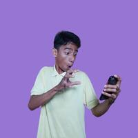 Young asian man surprised looking at smart phone, wearing yellow t-shirt, isolated pink background. photo