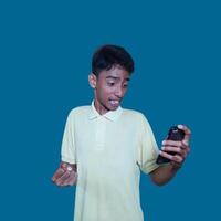 Young asian man surprised looking at smart phone, wearing yellow t-shirt, isolated pink background. photo