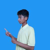 excited asian man wearing yellow t-shirt pointing to the copy space on the side, isolated blue background. photo