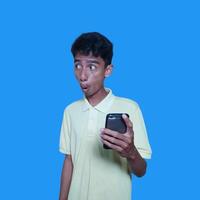 joven asiático hombre sorprendido mirando a inteligente teléfono pantalla, púrpura antecedentes. foto