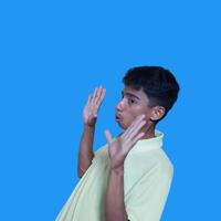 young asian man hands stop. with a serious face wearing a yellow t-shirt, isolated on a blue background photo