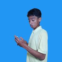 Young asian man surprised looking at smart phone isolated blue background. wearing a yellow t-shirt photo