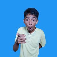 excited asian man wearing yellow t-shirt pointing to the camera blue background. photo