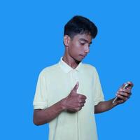 asiático hombre sonriente cara y o llave gesto.aislado en azul antecedentes. mientras participación un inteligente teléfono foto