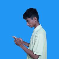 Young asian man surprised looking at smart phone isolated blue background. wearing a yellow t-shirt photo