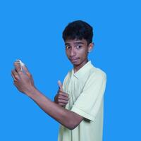 Young asian man surprised looking at smart phone isolated blue background. wearing a yellow t-shirt photo