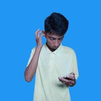 Young asian man surprised looking at smart phone isolated blue background. wearing a yellow t-shirt photo