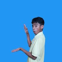 excited asian man wearing yellow t-shirt pointing to the copy space on the side blue background. photo